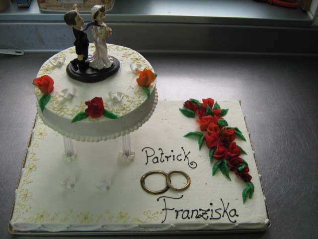 Zweistöckige Hochzeitstorte mit Brautpaarfigur und roten Rosen von Konditorei & Café Krüsmann Leipzig